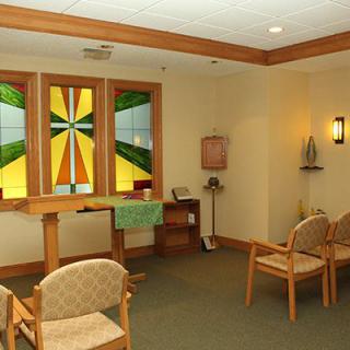 A peaceful chapel with stained glass windows and wooden chairs arranged for prayer.