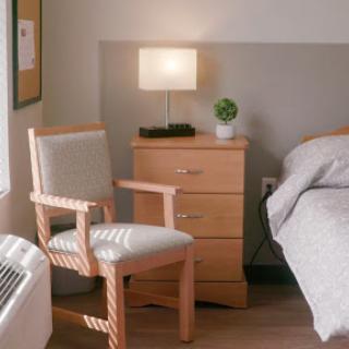 A cozy bedroom setting featuring a sleek chair, bedside table with a lamp, and a touch of greenery.