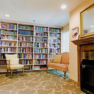 A cozy home library featuring bookshelves filled with books, comfortable armchairs, and a fireplace.