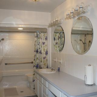 A well-lit bathroom with a shower, sink, and floral curtain.