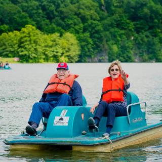 Two people enjoying a paddleboat ride on a lake surrounded by lush greenery.