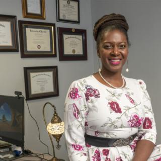 A woman standing in an office with certificates on the wall.