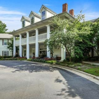 A colonial-style residential building with a large front porch and surrounding greenery.