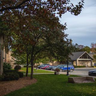 A quiet suburban neighborhood street lined with houses, trees, and parked cars on an overcast day.