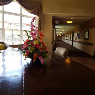 A beautifully arranged flower centerpiece on a wooden table in a hotel lobby, with large windows letting in natural light and a hallway visible in the background.
