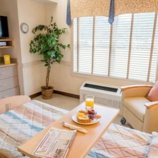 A bright hospital recovery room with a bed, meal tray, and comfortable seating.