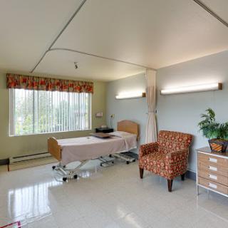 A well-lit hospital room featuring a patient bed, comfortable chair, and a view outside.