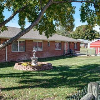 A brick house with a well-maintained lawn, featuring a tree and a fountain in the front yard.