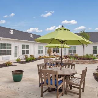 A courtyard featuring a wooden table set with green umbrellas against a backdrop of a white building and blue sky.