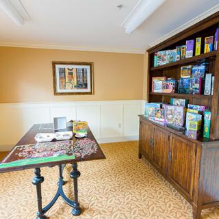 A cozy puzzle room featuring a table with an ongoing jigsaw puzzle and a bookcase filled with board games and puzzles.