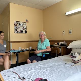 A patient enjoys the company of a caregiver and a dog in a hospital room.