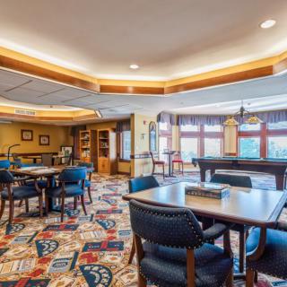 A spacious and well-lit lounge area featuring tables, chairs, and a pool table on a colorful carpet.