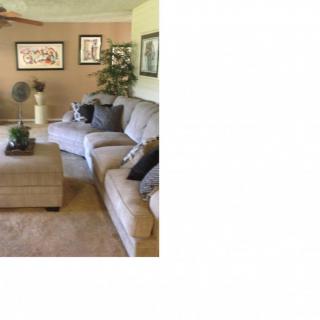 A cozy living room featuring a soft gray sofa, a matching ottoman, decorative pillows, wall art, and a potted plant.