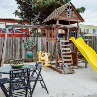 A backyard playground featuring a wooden swing set with a slide, alongside an outdoor table and chairs.