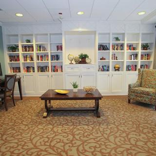A cozy library space featuring built-in bookshelves, a central coffee table, and comfortable seating.