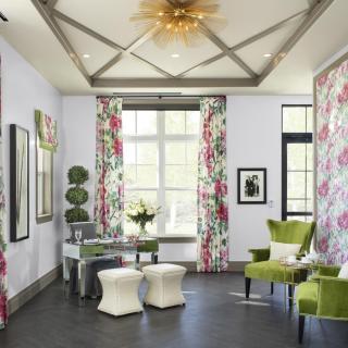 A stylish living room featuring floral curtains and green chairs, complemented by modern decor and ample natural light.
