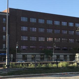 A multi-story brick building with large windows, located in an urban setting during the daytime.