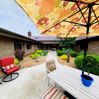 A cozy courtyard with a patio set under a floral umbrella, surrounded by well-maintained landscaping.