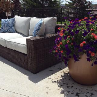 A comfortable patio sofa with cushions next to a vibrant potted flower arrangement on a sunny terrace.