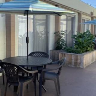 An outdoor patio area with a round table, chairs, and an umbrella, next to some greenery.