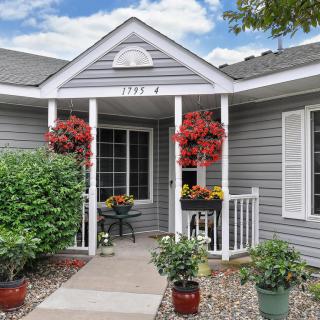 A charming house entrance with gray siding, featuring a welcoming front porch adorned with hanging and potted plants.