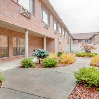 A view of a courtyard with landscaping, featuring shrubs and a concrete sidewalk in front of a brick building.