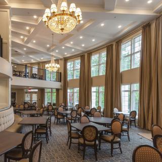 A spacious dining area with elegant chandeliers, large windows, and neatly arranged tables and chairs.