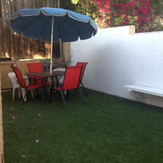 A cozy backyard patio with a table, chairs, and an umbrella on a grassy area.
