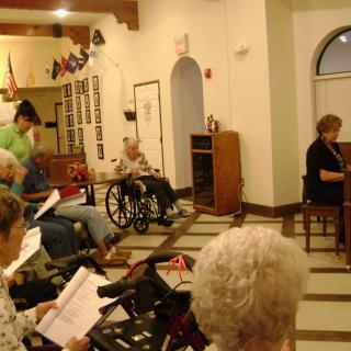 A group of seniors gathered in a communal area, some in wheelchairs, engaging in an activity.