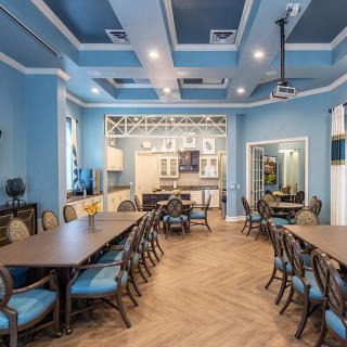 A spacious dining room with blue walls, elegantly arranged tables and chairs, featuring a modern ceiling design and wooden flooring.