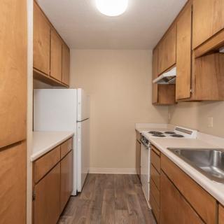 A compact kitchen with wood cabinets and essential appliances including a refrigerator, oven, and sink.