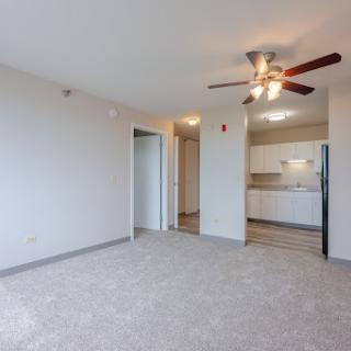 A spacious living room area featuring a ceiling fan and open access to the kitchen.