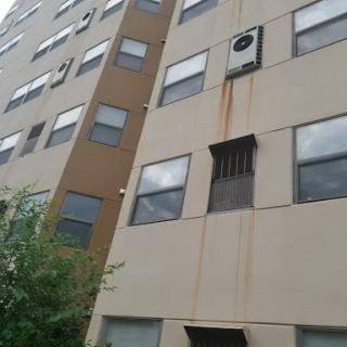 An exterior view of an apartment building featuring multiple windows and an air conditioning unit.