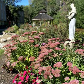 A serene garden with a statue, vibrant flowers, and a gazebo in the background.