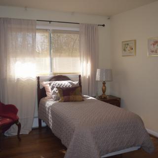 A cozy bedroom with a single bed, bedside lamp, and soft natural light filtering through the curtains.
