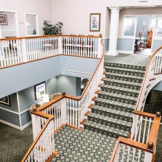 A spacious building interior featuring a grand staircase with carpet and wooden banisters.
