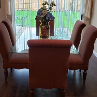 A dining area featuring a glass-top table and four upholstered chairs, adorned with a decorative vase and flowers.