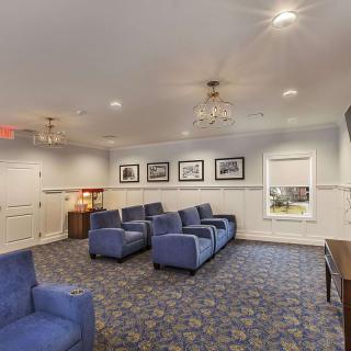 A cozy living room with blue chairs, chandeliers, and framed pictures on the wall.