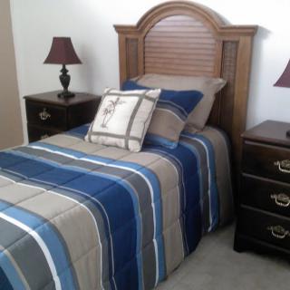 A cozy bedroom featuring a single bed with striped bedding and matching pillows, accompanied by nightstands and lamps on either side.