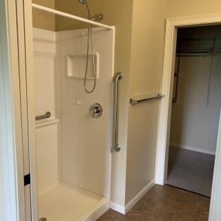 A modern walk-in shower with grab bars and an adjacent closet.