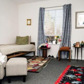 A cozy bedroom interior with a single bed, decorated with colorful rugs and framed art.