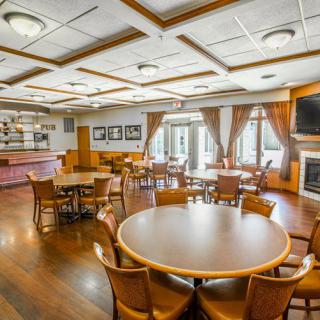 A spacious dining area with round tables, wooden flooring, and warm lighting, creating a cozy atmosphere.