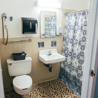 A small bathroom with a toilet, sink, and shower, featuring a patterned shower curtain and tiled floor.