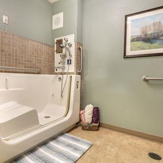 A bathroom featuring an accessible walk-in tub with safety features such as grab bars, a tiled wall, and a nearby towel basket.