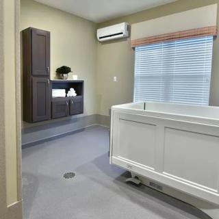 A modern bathroom interior featuring a walk-in bathtub, cabinetry, and window blinds under an air conditioning unit.