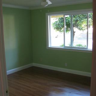 A view of an empty room with green walls, a large window, and wooden flooring.