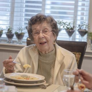 An elderly woman enjoying a meal at the dining table.