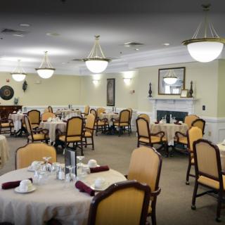 An elegant dining room with neatly arranged tables and chairs, featuring chandeliers and a fireplace.