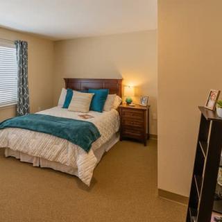 A cozy bedroom featuring a neatly made bed with teal accents, a bedside lamp on a nightstand, and a window with curtains.