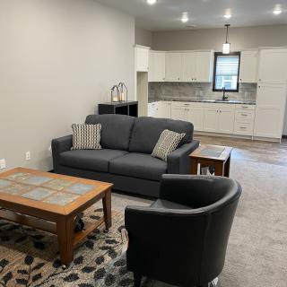A modern open-plan living room and kitchen with a comfortable sofa, armchair, and wooden coffee table.